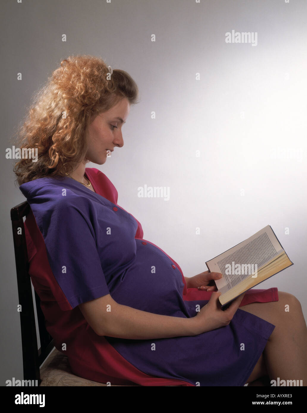 young girl, young woman, 20 to 25 years, portrait, brown, brunette, long hair, sitting on a chair, reading a book, read, reader, pregnant, expectant, far advanced in pregnancy, pregnancy, pensive, pensiveness, thoughtful, lost in thought, think, thinking Stock Photo