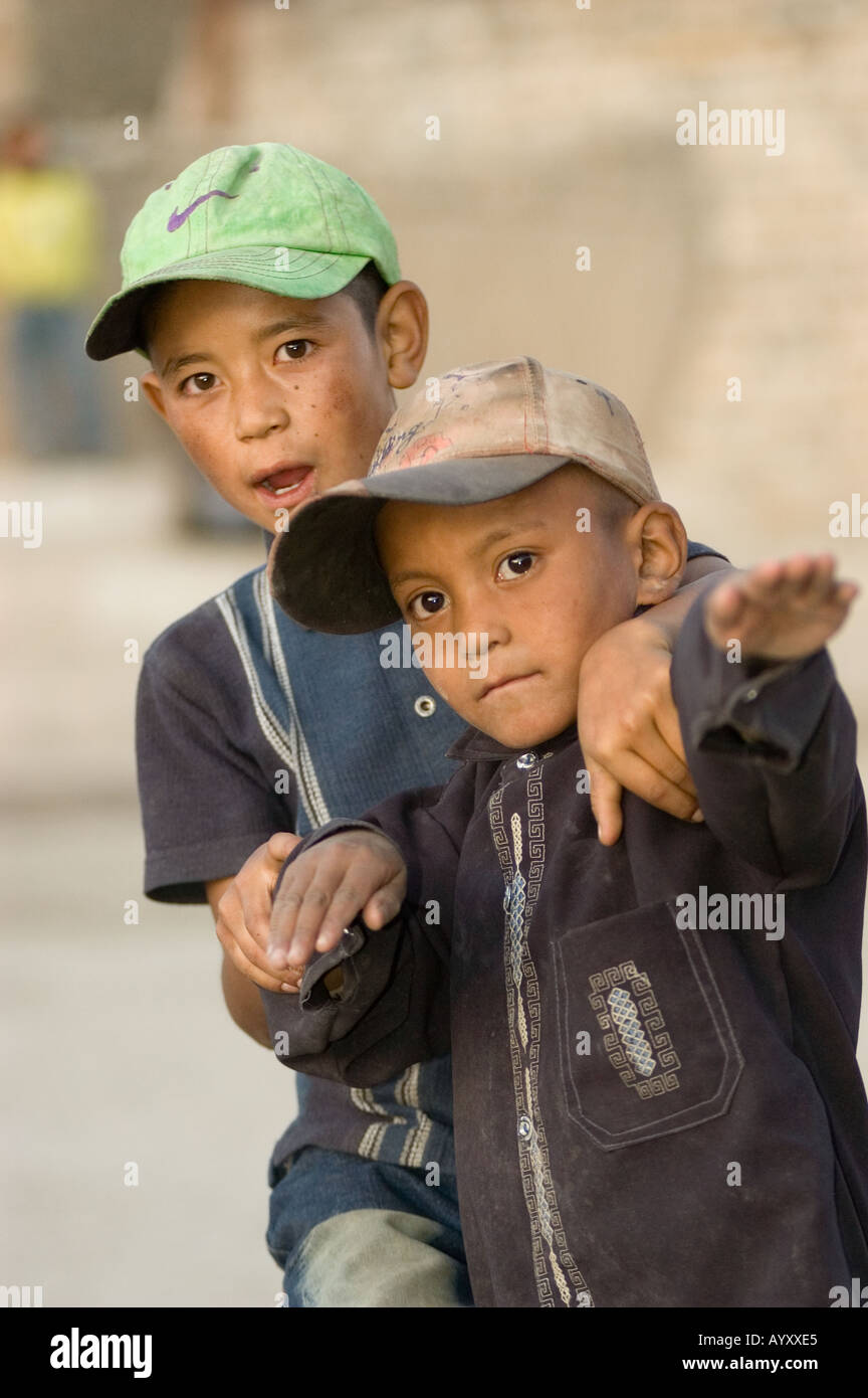 Two curious Ladakhi boys with modern dress and caps looking at camera ...