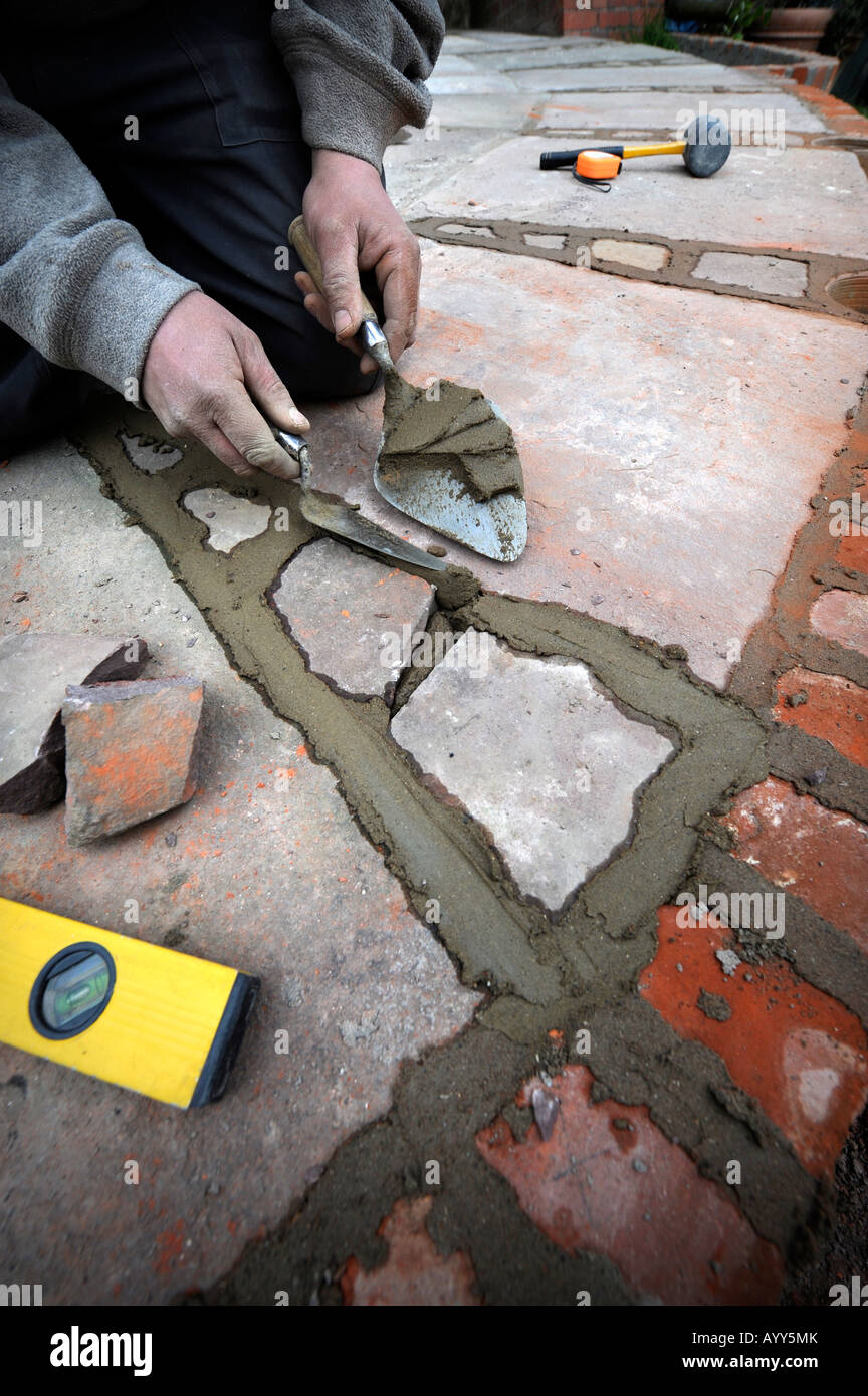 A BUILDER POINTING IN A PATIO LAID WITH NATURAL STONE SLABS UK Stock