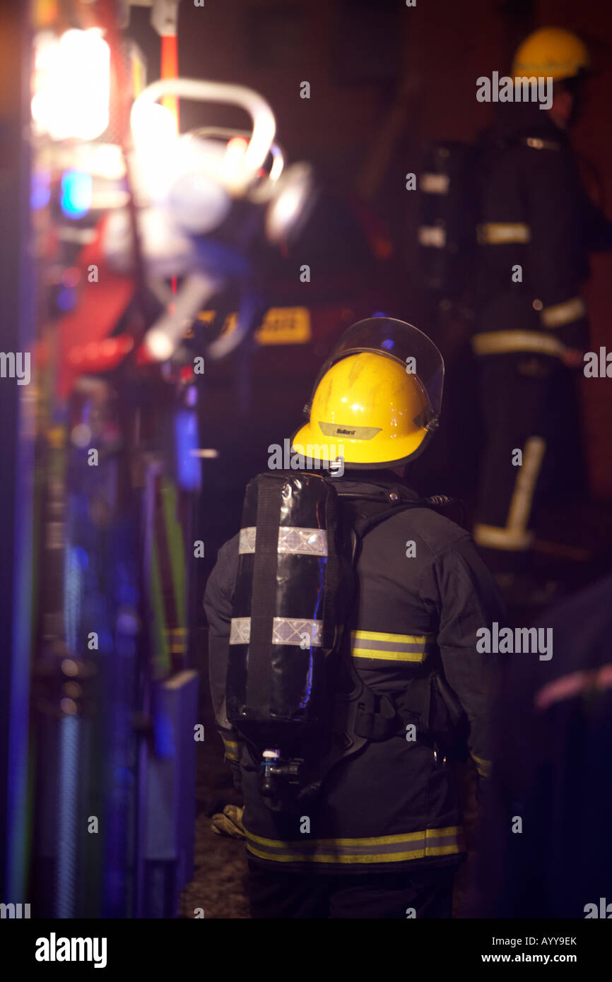 firefighter wearing breathing apparatus waits at the rear of a fire tender truck at the scene of a house fire in the uk Stock Photo