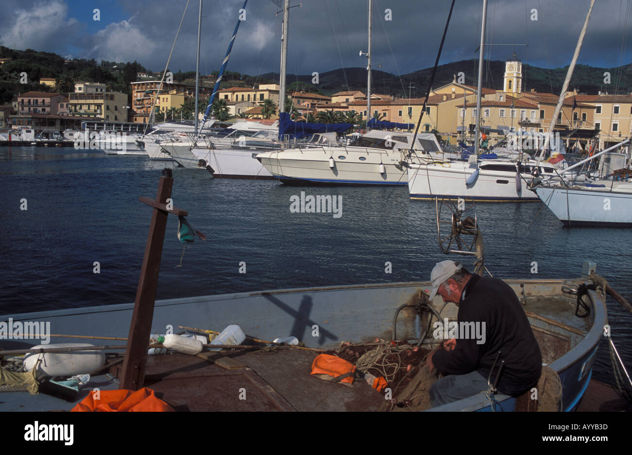Fisherman commercial mending net in skiff in harbor of town Porto Azzurro Island Elba Italy Stock Photo