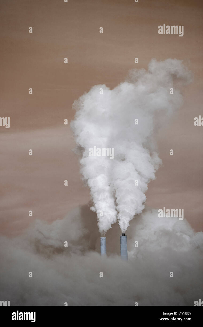 surrounded by a brown haze, a coal-burning electrical generating plant emits steam from its two smokestacks. Stock Photo