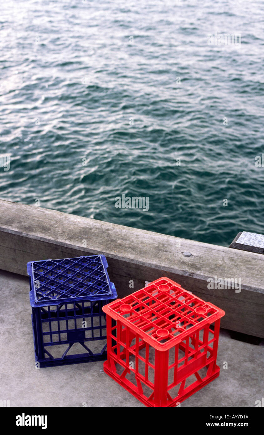 Two plastic empty milk crates blue and red on the edge of a harbour wharf  next to the water Stock Photo - Alamy