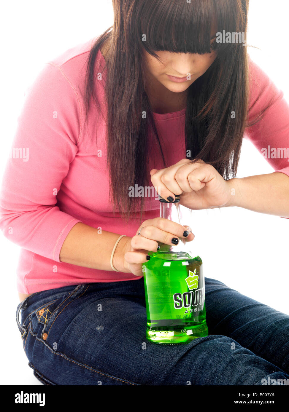Young Underaged Teenage Girl Sitting On The Floor Alone Experiencing  Inflicted Alcohol Abuse Drinking Alcohol Wearing A Pink Top And Blue Denim Jeans Stock Photo