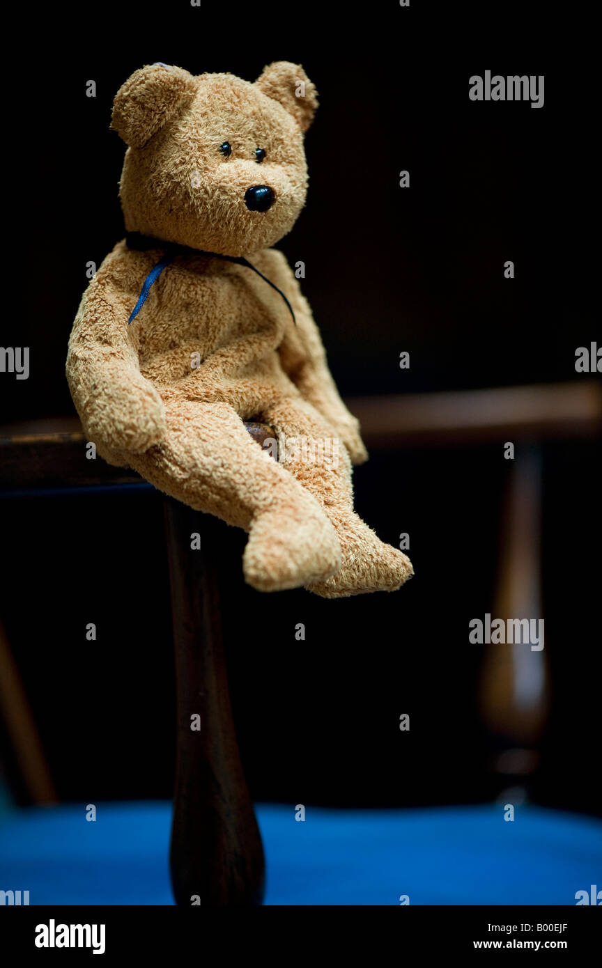 Teddy bear sitting on antique wooden chair Stock Photo
