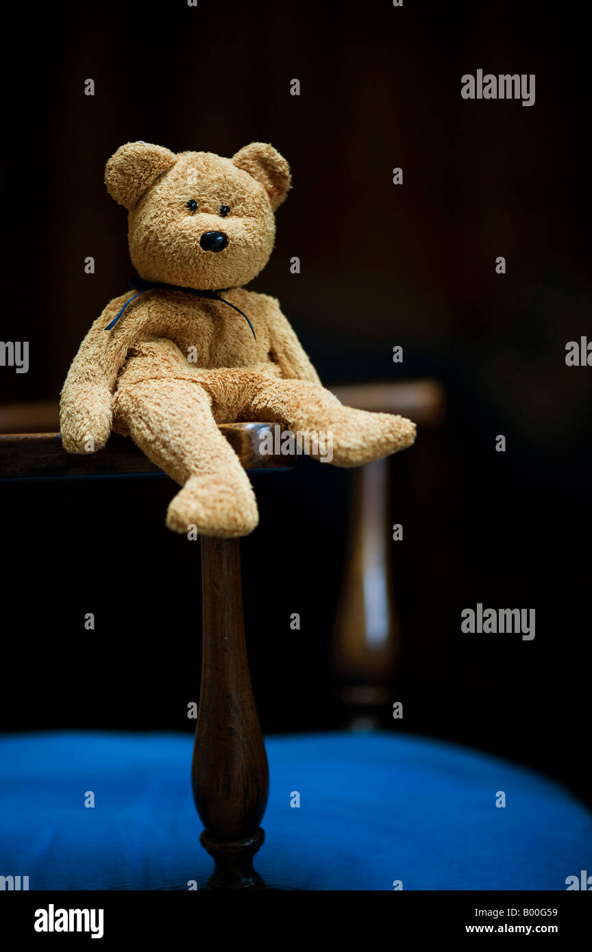 Teddy bear sitting on antique wooden chair Stock Photo