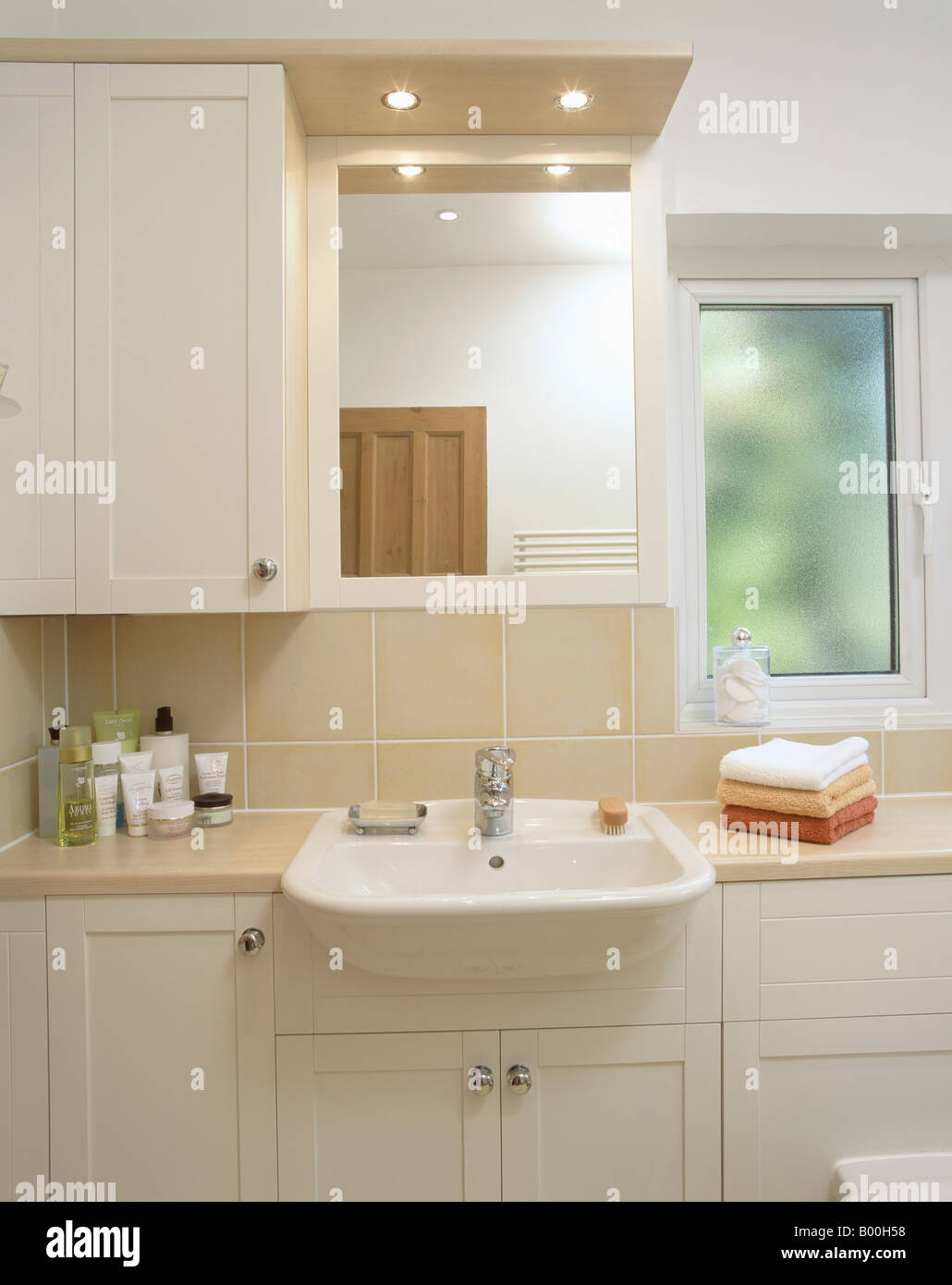 Downlighting above mirror and white basin built into fitted vanity unit