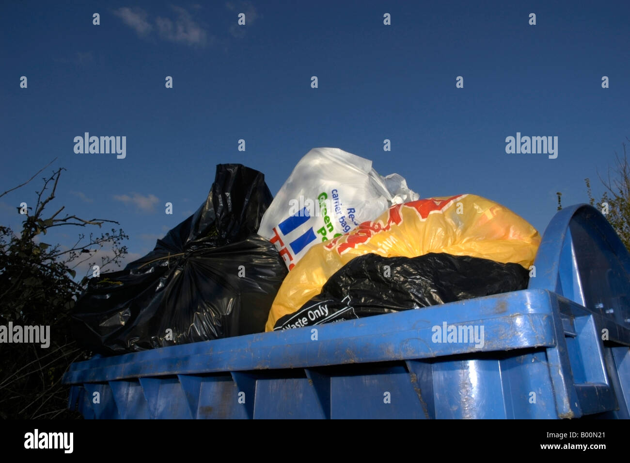 Blue commercial wheely bin overflowing with plastic bags of rubbish