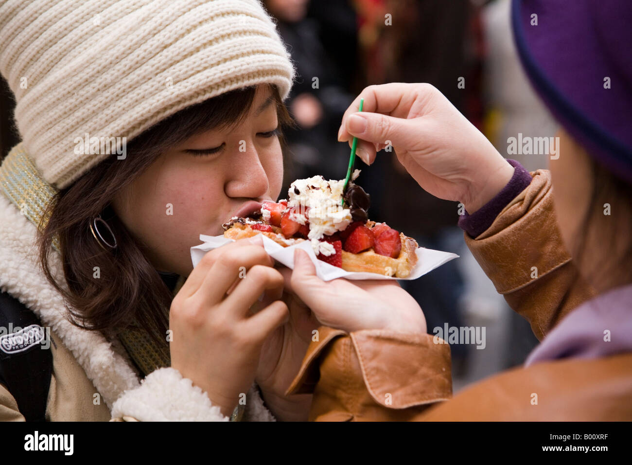 Japanese woman tourist being fed a Belgian waffle with strawberries and whipped cream, in Brussels, Belgium. Stock Photo