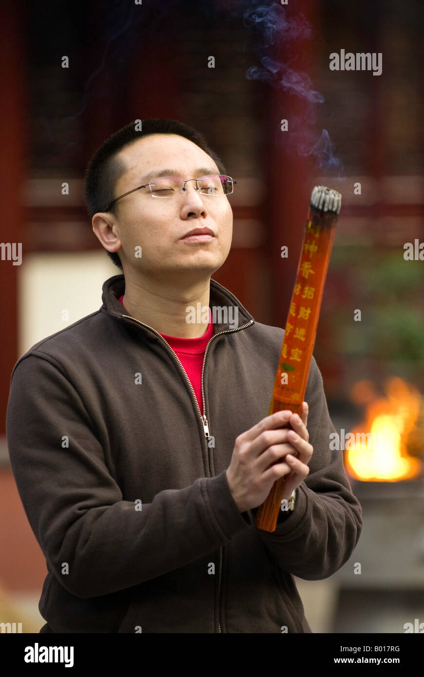 Contemporary dressed young man offers burning incense and prays at