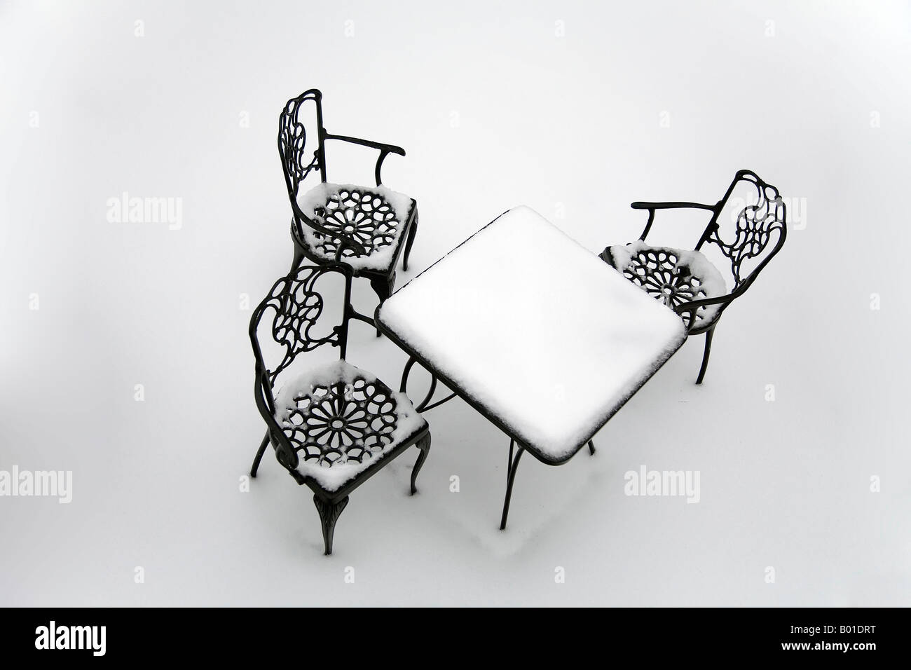 Three chairs arranged around a table are all covered by snow Stock Photo