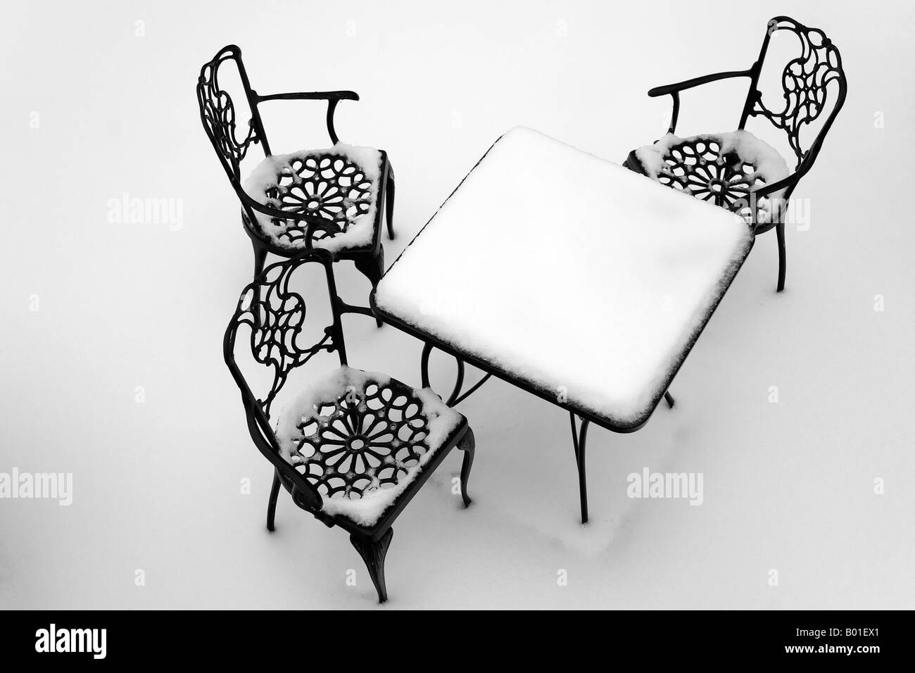 Three chairs arranged around a table are all covered by snow Stock Photo