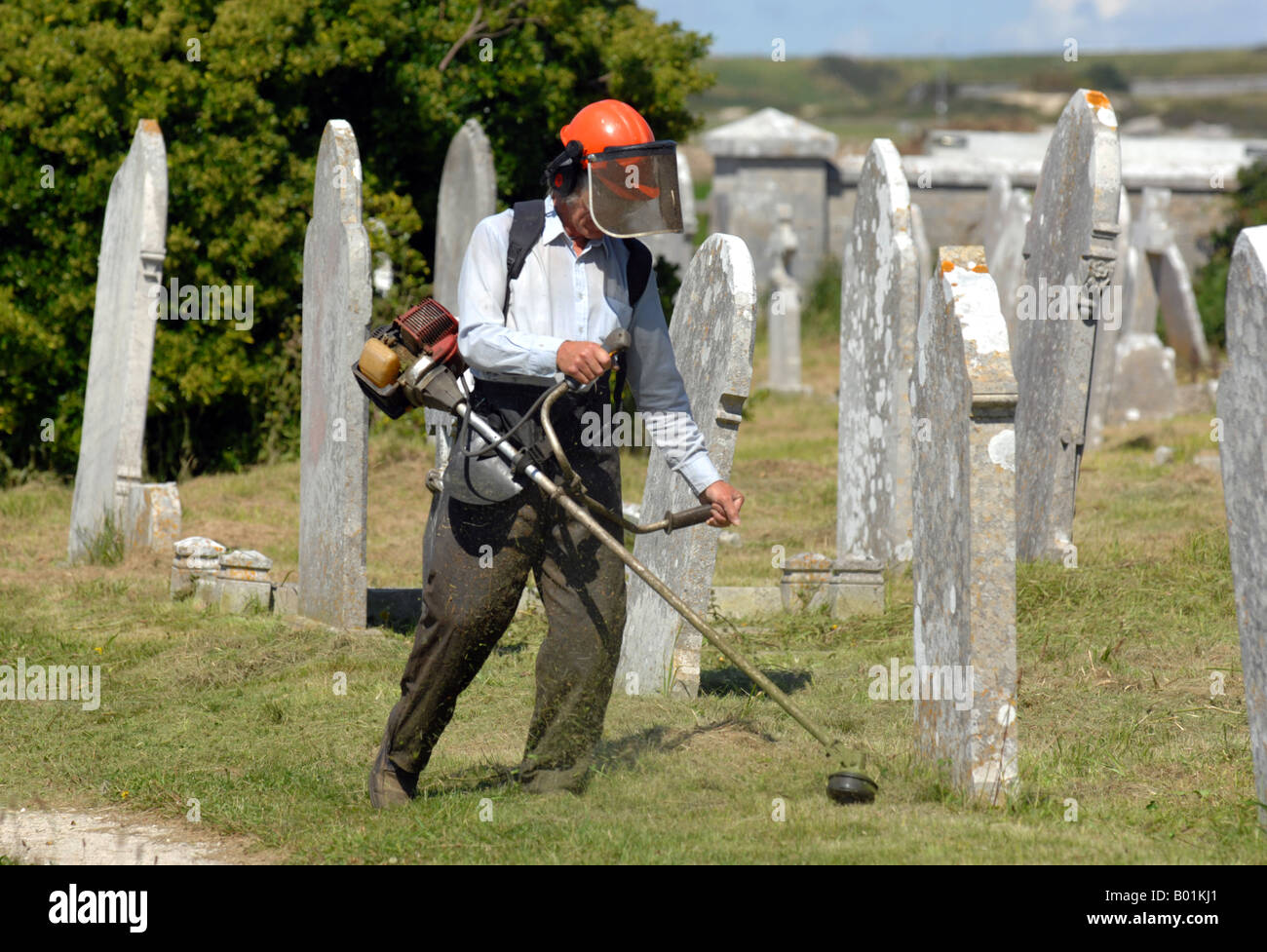 Workman cuts grass in a cemetery Stock Photo