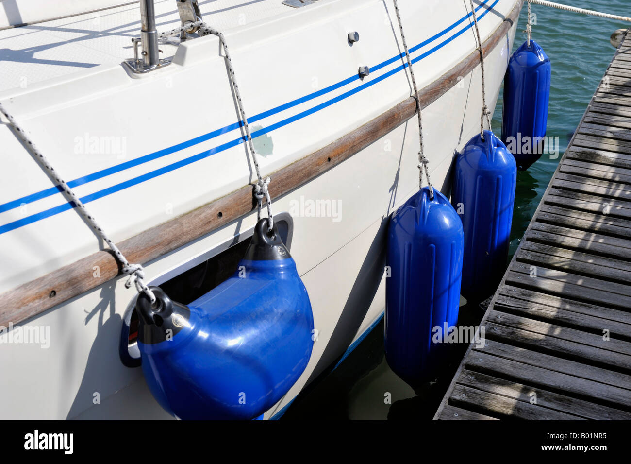 blue plastic fenders hanging down on side of moored boat Stock Photo