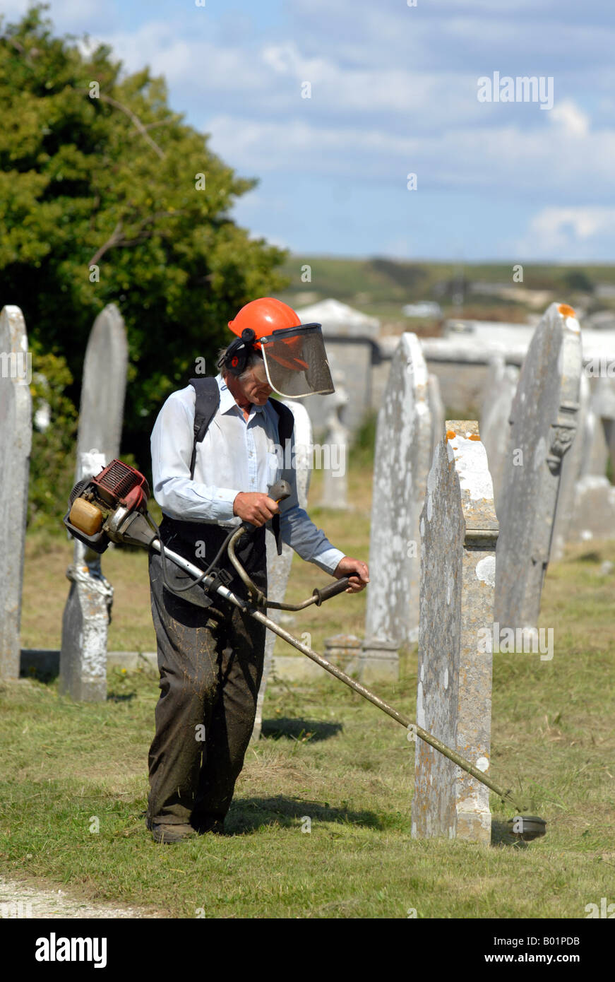 Workman cuts grass in a cemetery Stock Photo