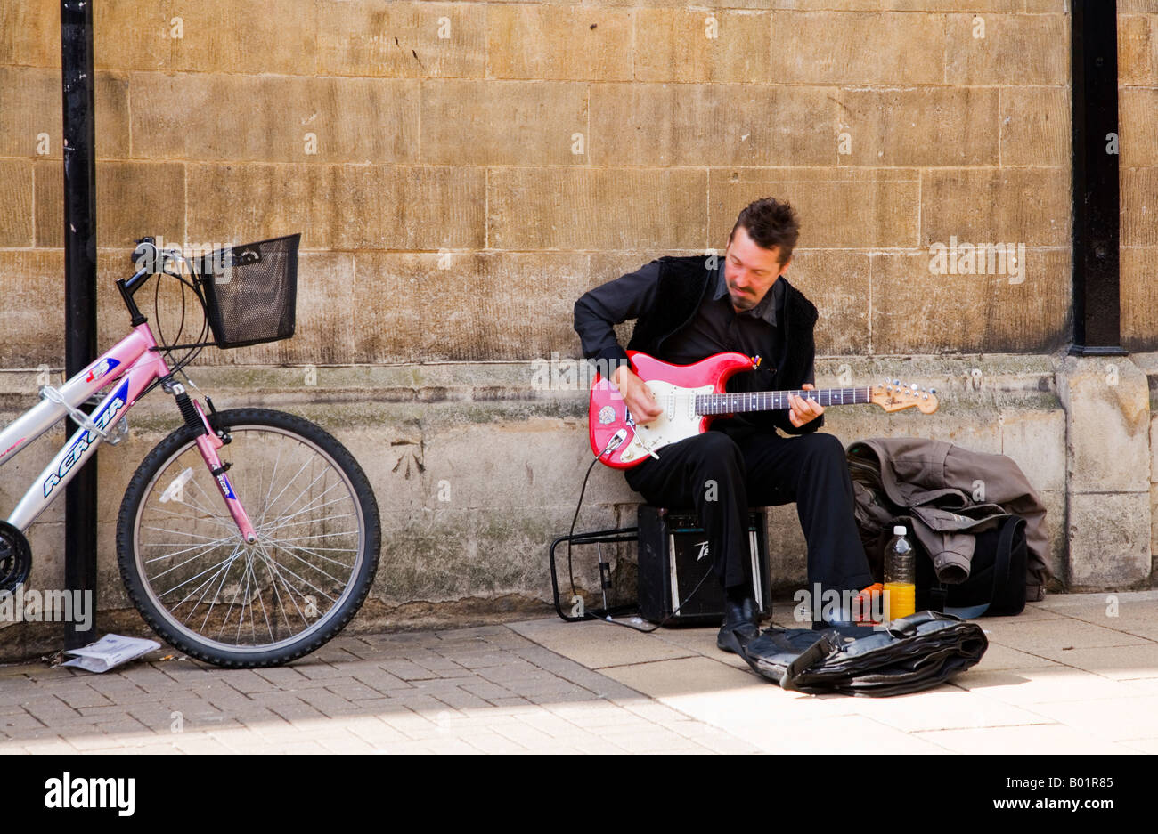 Man, busker, playing electric guitar, busking, sitting by a wall in