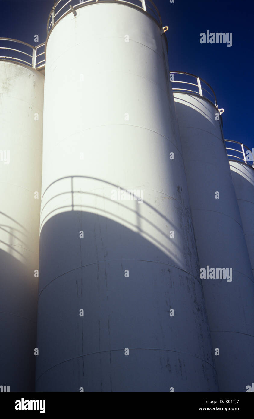 View from below of large industrial chemical or petroleum storage tanks with shadows of other tanks and blue sky Stock Photo