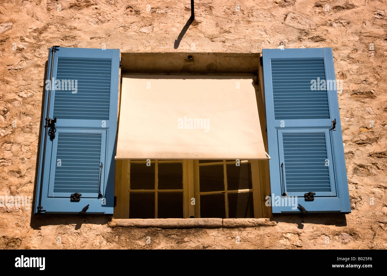 Window with blue shutters and canvas awning in a stone wall in St Paul