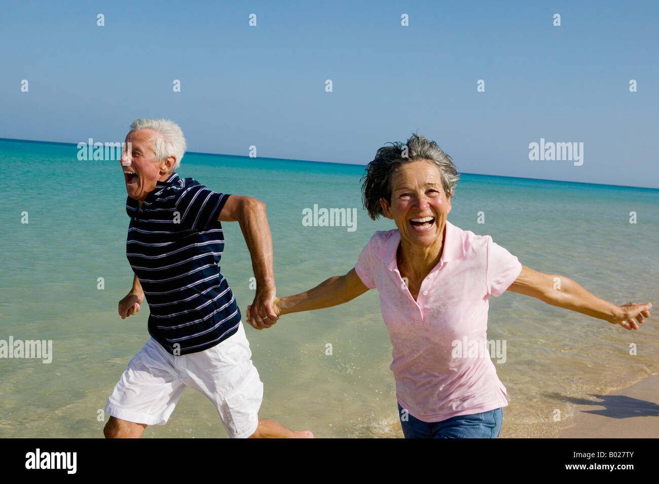 mature couple running along beach hand in hand Stock Photo - Alamy