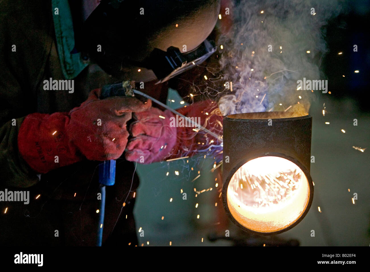 Arc welder wearing special protective equipment repairs gas transmission pipe in factory. Stock Photo