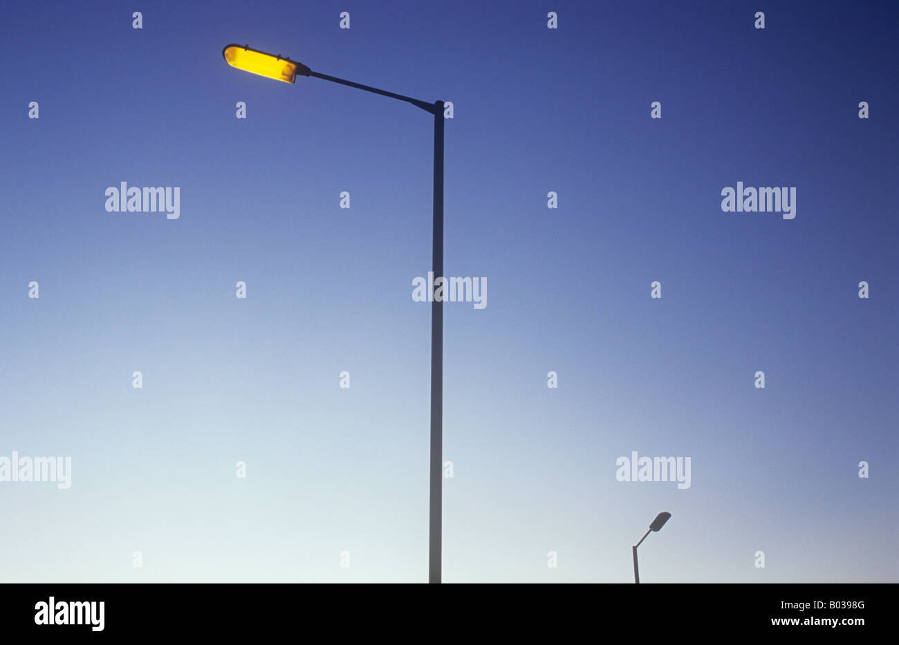Tall slender street lamp glowing orange against mauve early evening sky  with distant lamp not yet switched on Stock Photo - Alamy