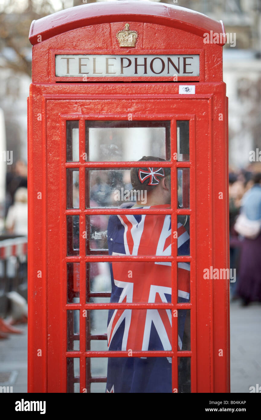 A man wearing a Union Jack flag in a distinctive red telephone box