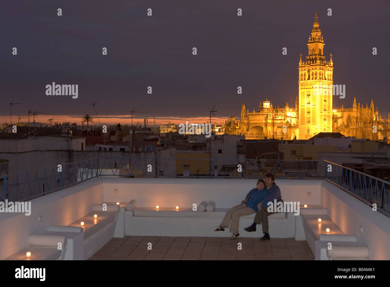 Couple on the terrace at Banos Arabes-Aire de Sevilla with La Giralda and Sevilla Cathedral in background at dusk Stock Photo