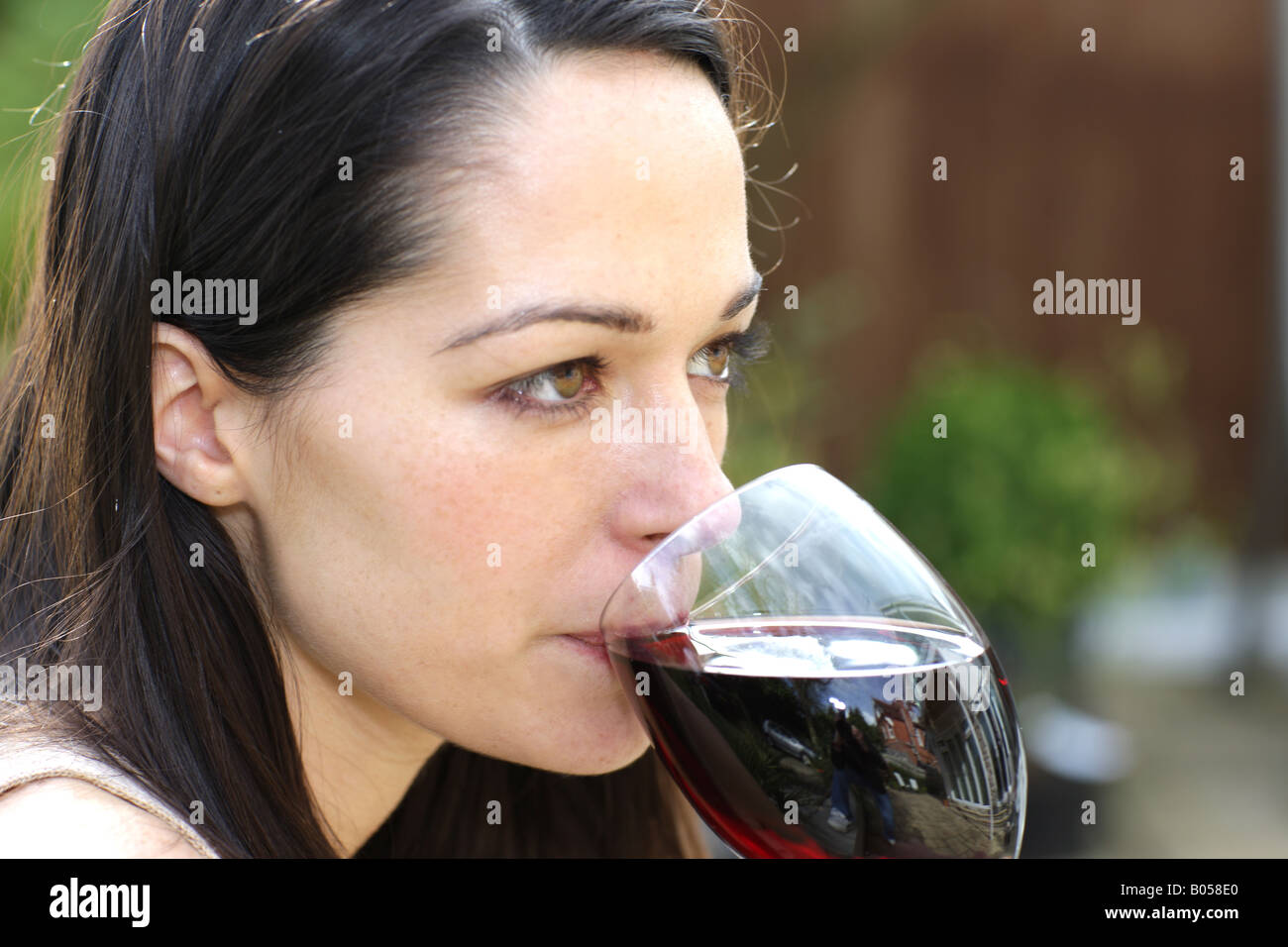 Young Woman Sitting In Her Garden Alone Holding And Drinking A Glass Of Red Wine Stock Photo