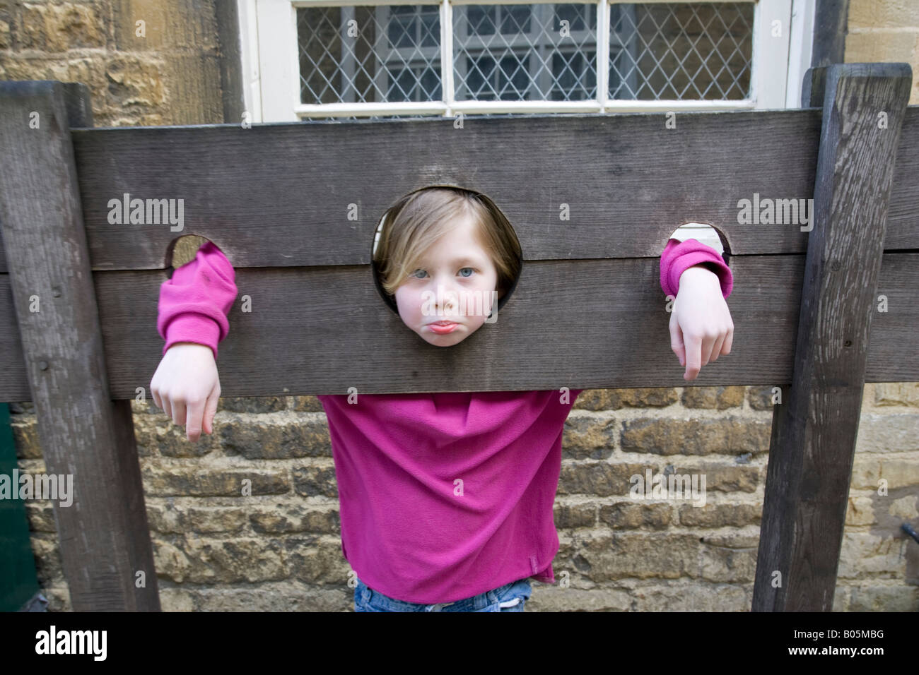 Young girl in wooden medieval stocks Bourton on the Water UK Stock Photo