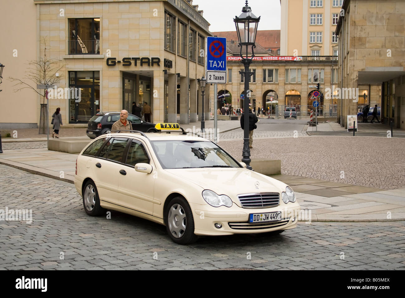 Taxi waiting by the curb on a cobblestone street in Dresden, with the G-Star store in the background and the Koenig-Johann-Denkmal visible Stock Photo