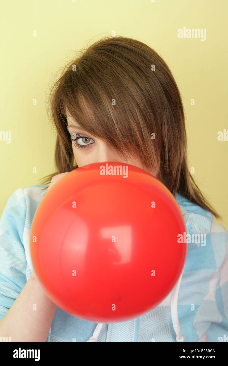 teenage girl blowing up a red balloon against a yellow background. Stock Photo