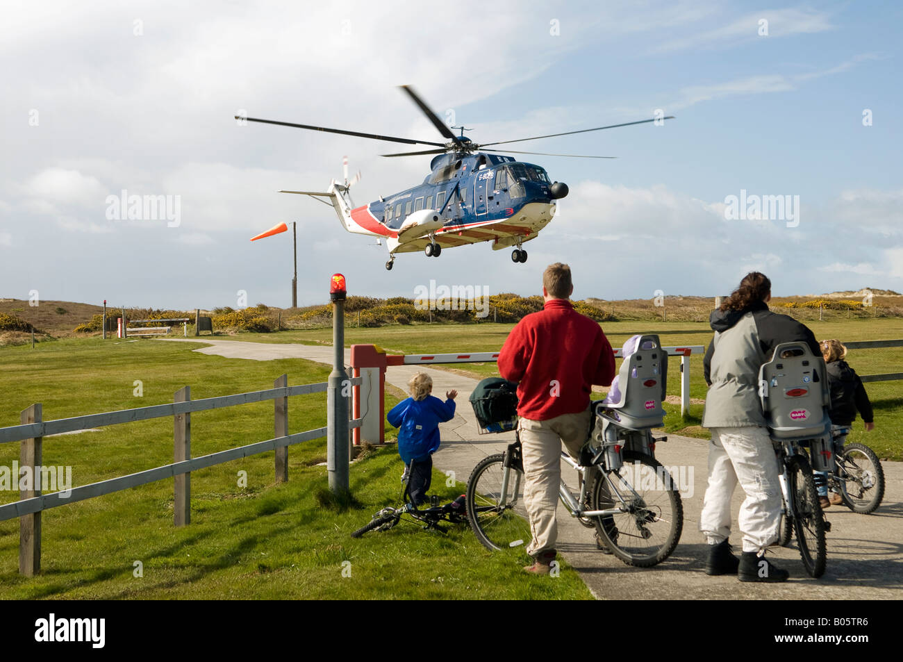 Family on bicycles, viewing helicopter taking off from Tresco heliport, Isle of Scilly. Stock Photo