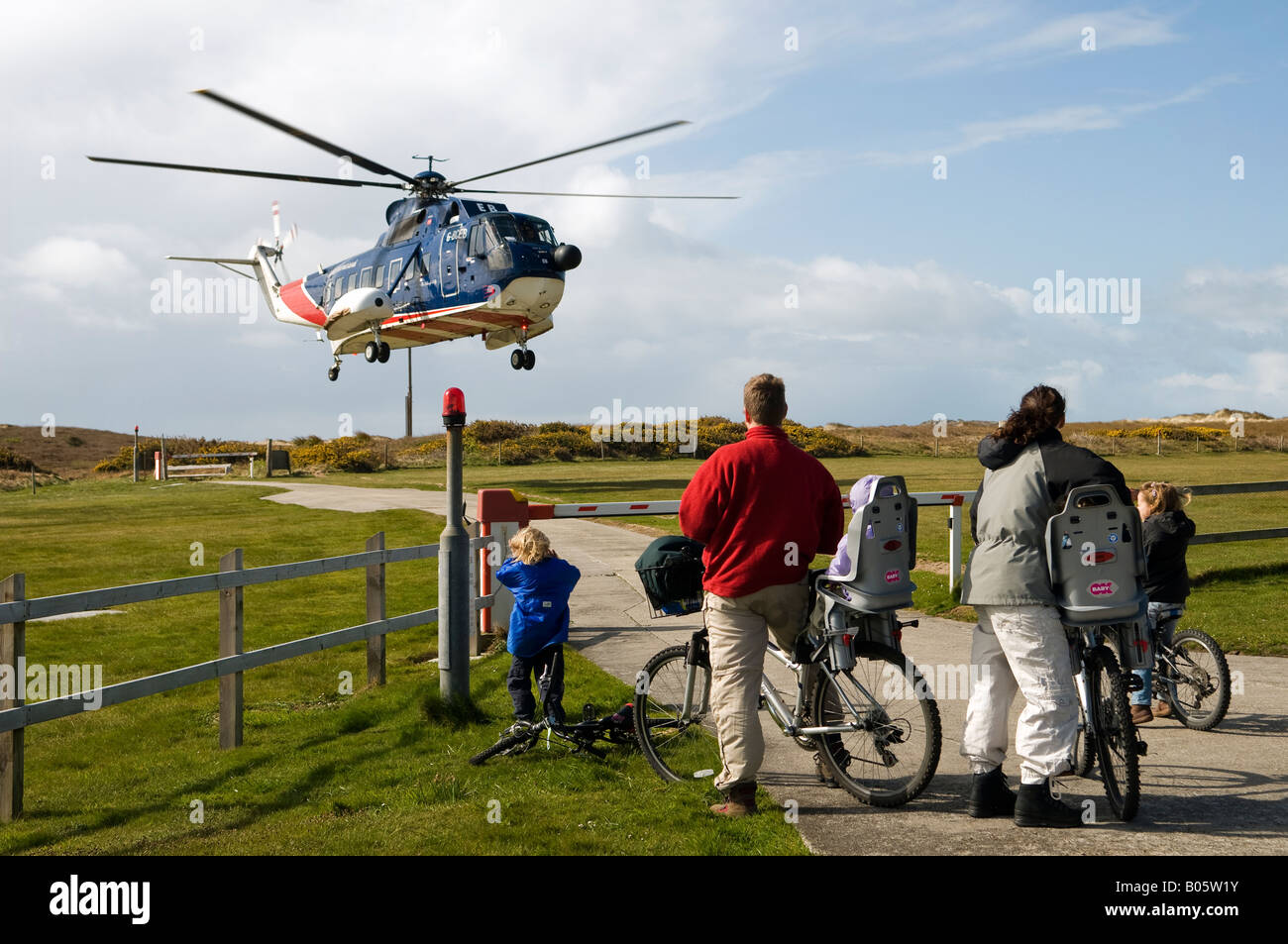 Family on bicycles, viewing helicopter taking off from Tresco heliport, Isle of Scilly. Stock Photo