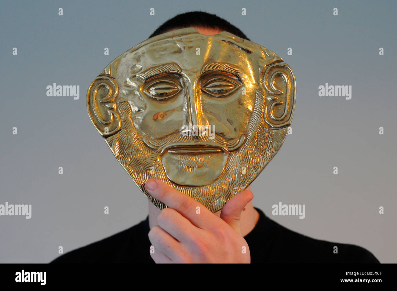 Young man hiding behind a replica Mask of Agamemnon, the replica is made of brass, the original is gold. Stock Photo