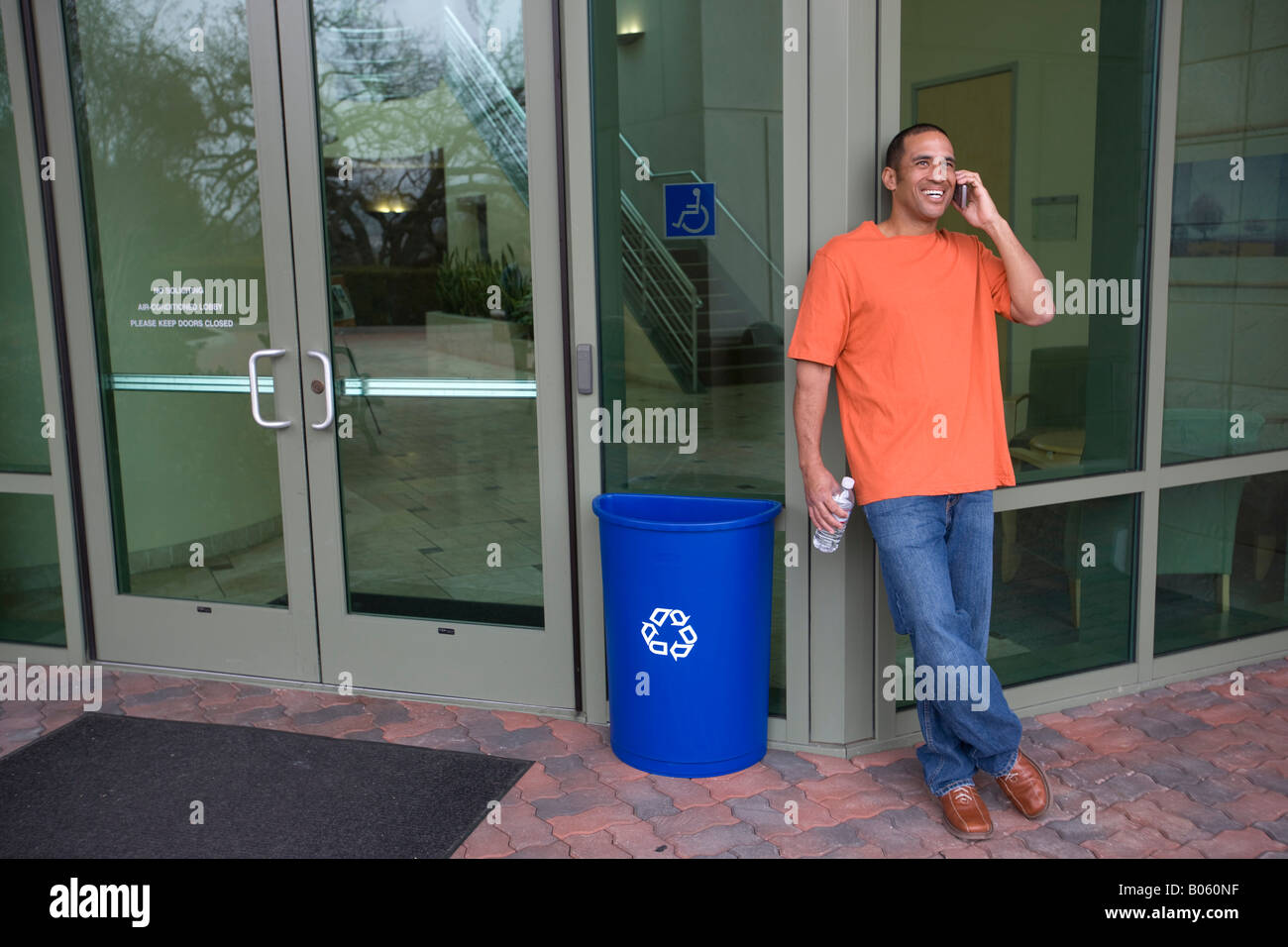 Casually dressed businessman drops empty plastic water bottle in recycling container outside office lobby Stock Photo
