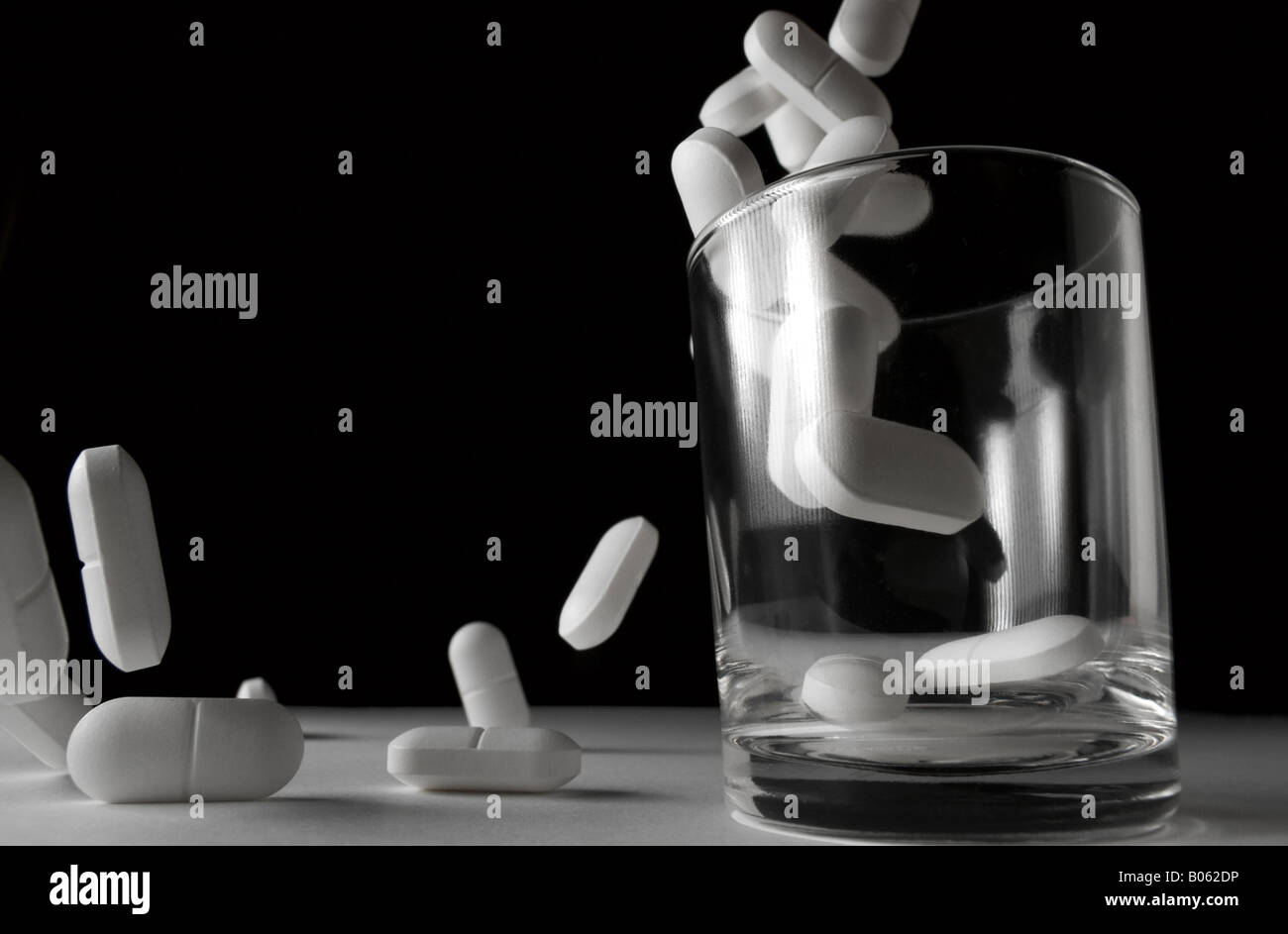 Pills falling to a glass and beyond Stock Photo