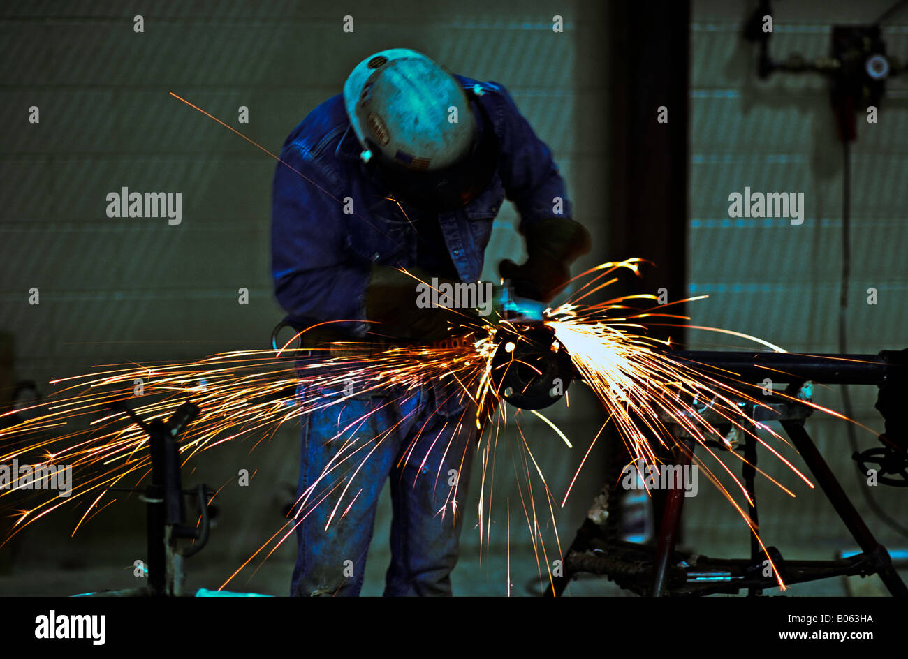 Male worker wearing appropriate safety equipment uses a grinder in the construction area of a piping fabrication plant Stock Photo