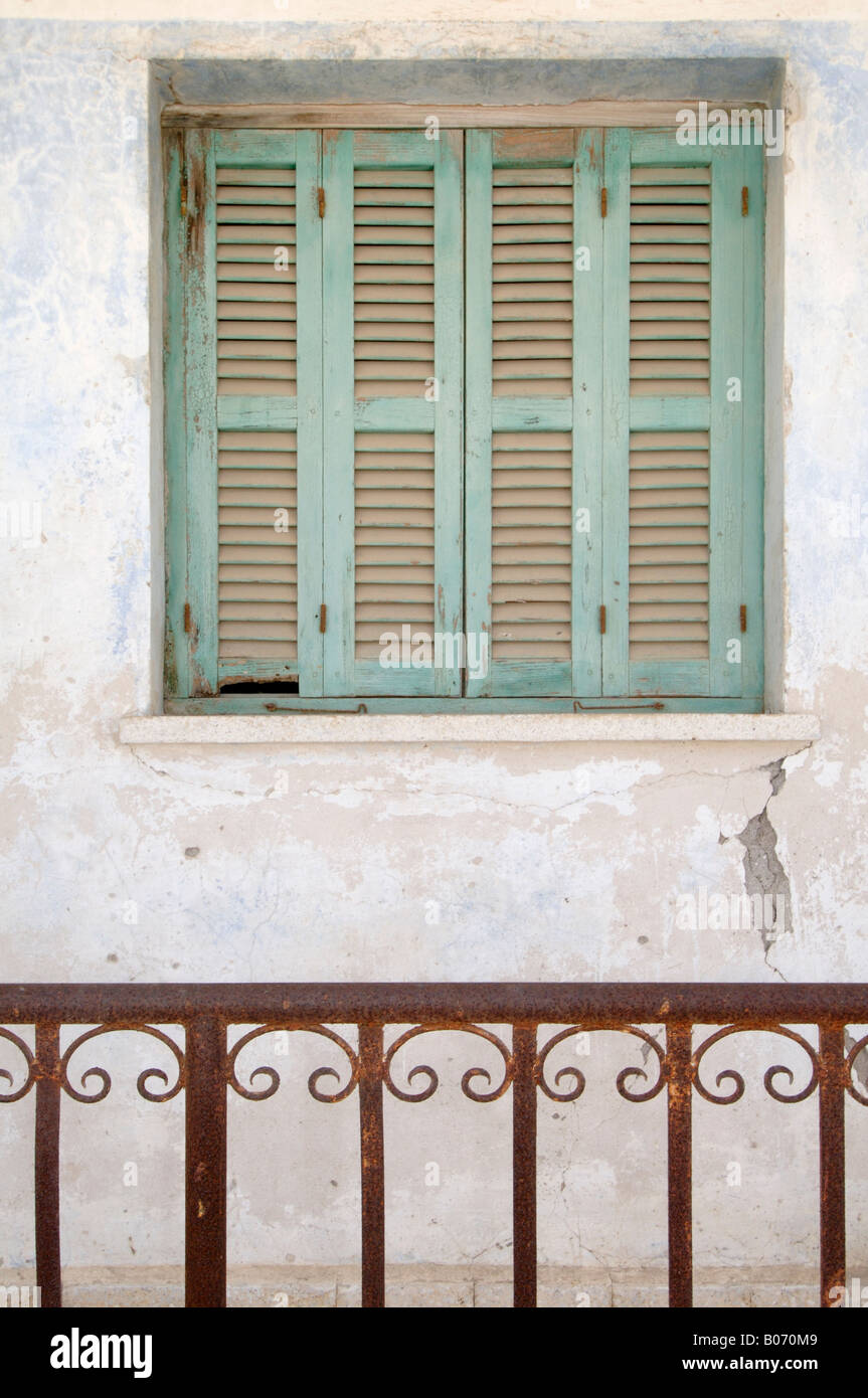 Faded green louvred shutters in a wall behind rusting ornate railings in the traditional village of Polemi, Paphos, Cyprus Stock Photo