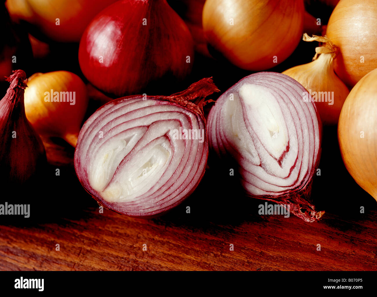 CUT RED ONION SURROUNDED BY WHOLE RED AND WHITE ONIONS ON A WOODEN SURFACE Stock Photo