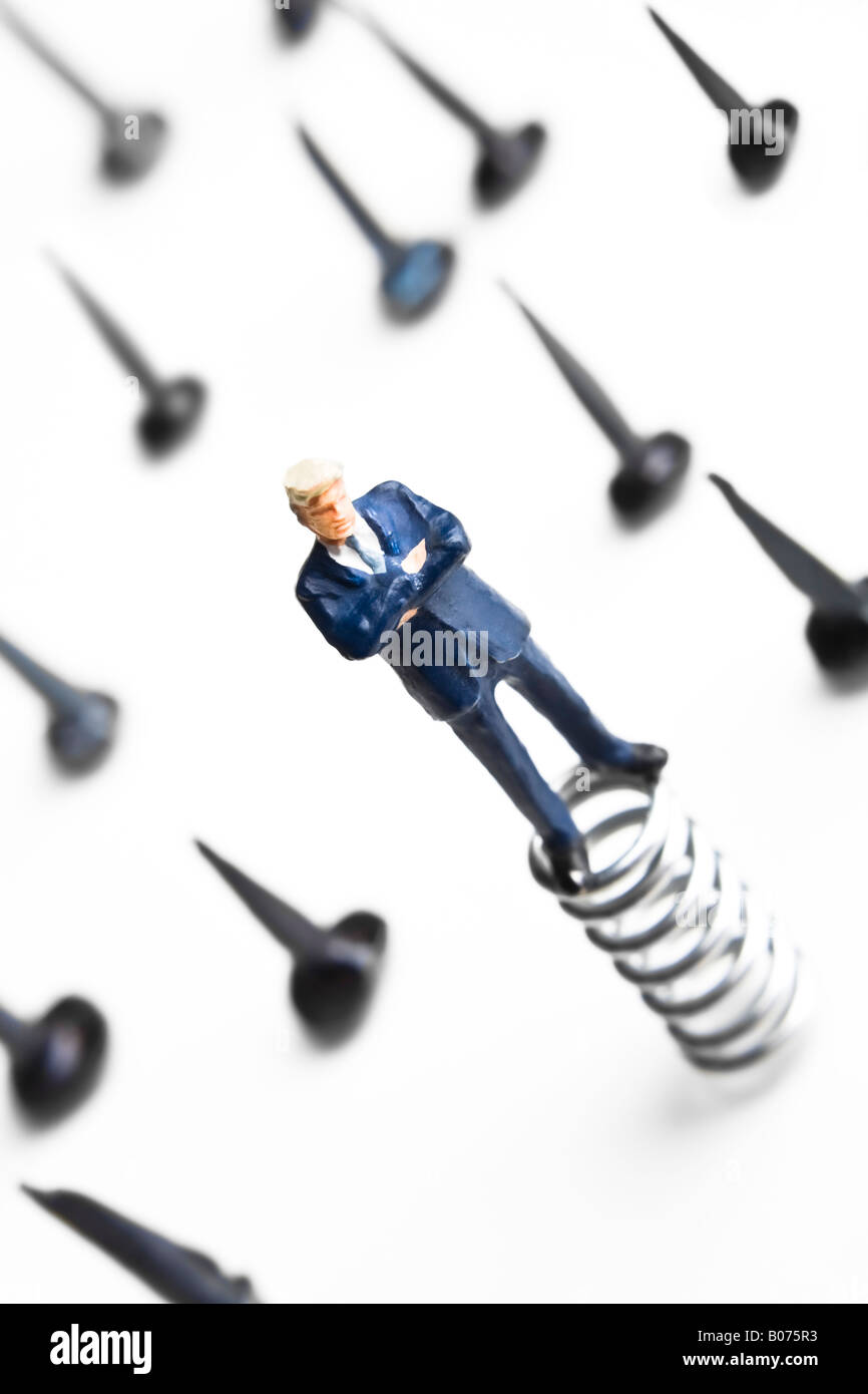 Figurines standing on springs surrounded by tacks Stock Photo