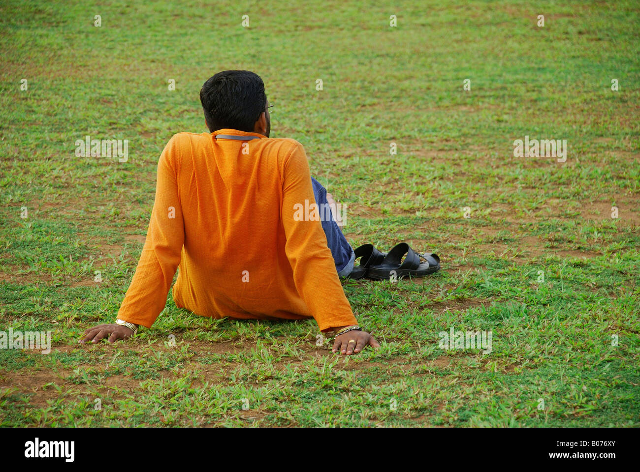 Young man in yellow shirt siting and relaxing on the grass Stock Photo