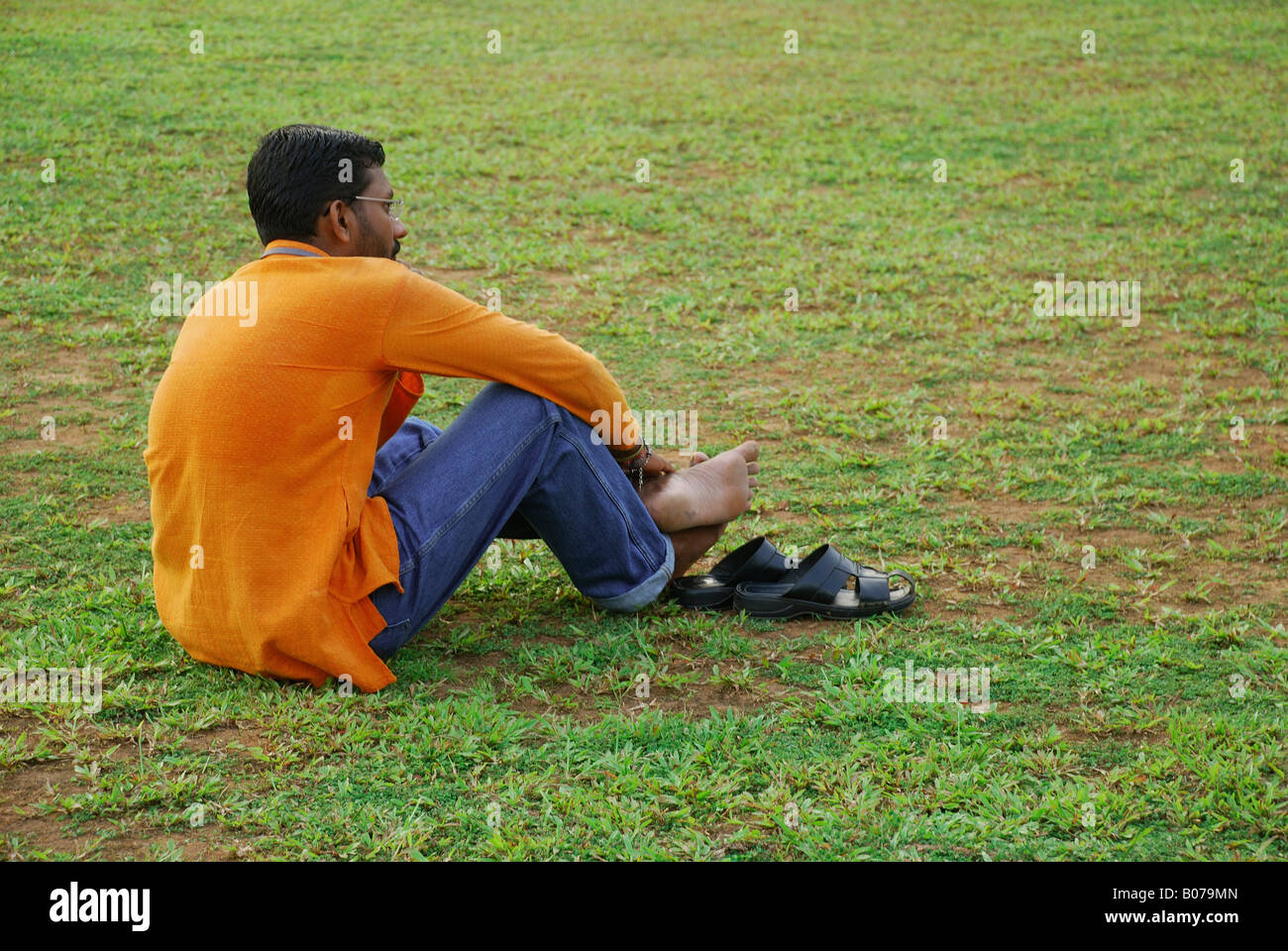 Young man in yellow shirt siting and relaxing on the grass Stock Photo