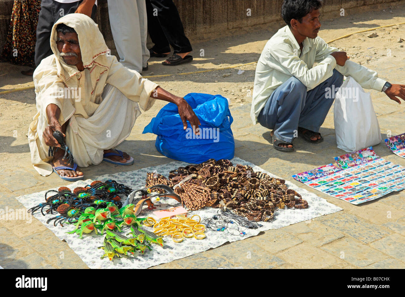 Two Indian street sellers squatting with souvenirs on pavement by the