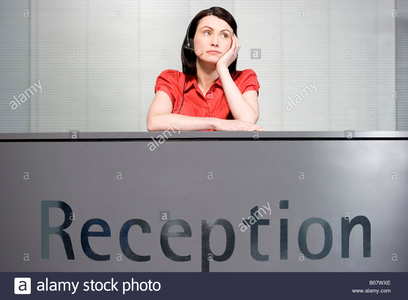 Office receptionist in a red blouse, looking bored Stock Photo