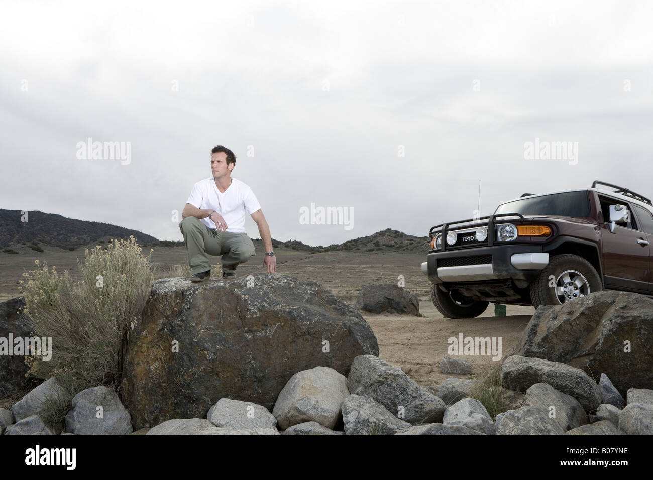 Man kneeling on rock on off-road area Stock Photo - Alamy