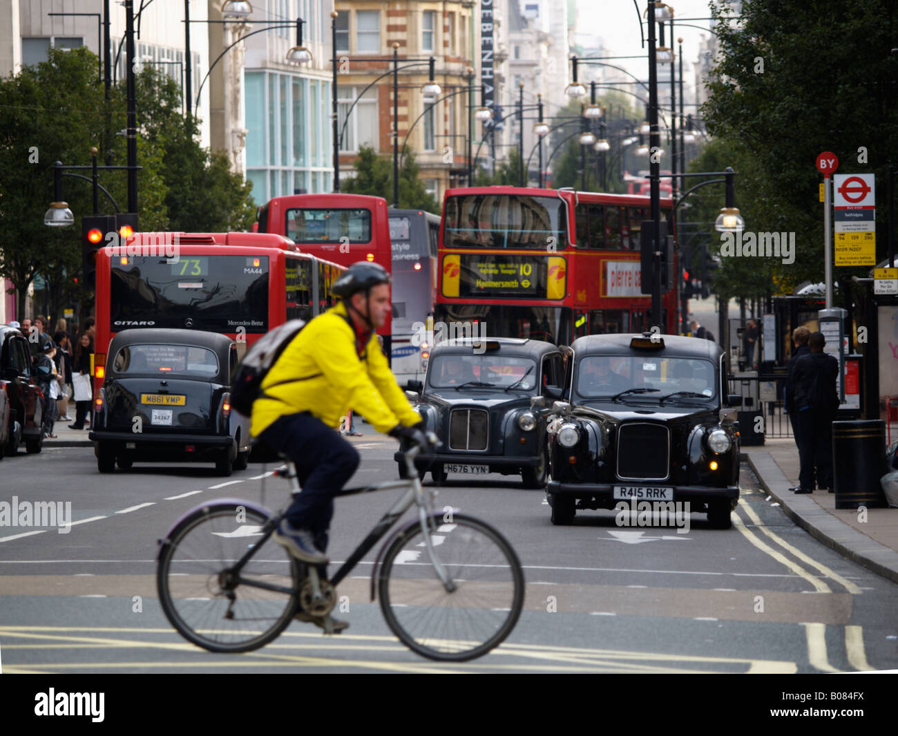 Bicyclist with yellow jacket and helmet crossing riding on Oxford Street London UK Stock Photo