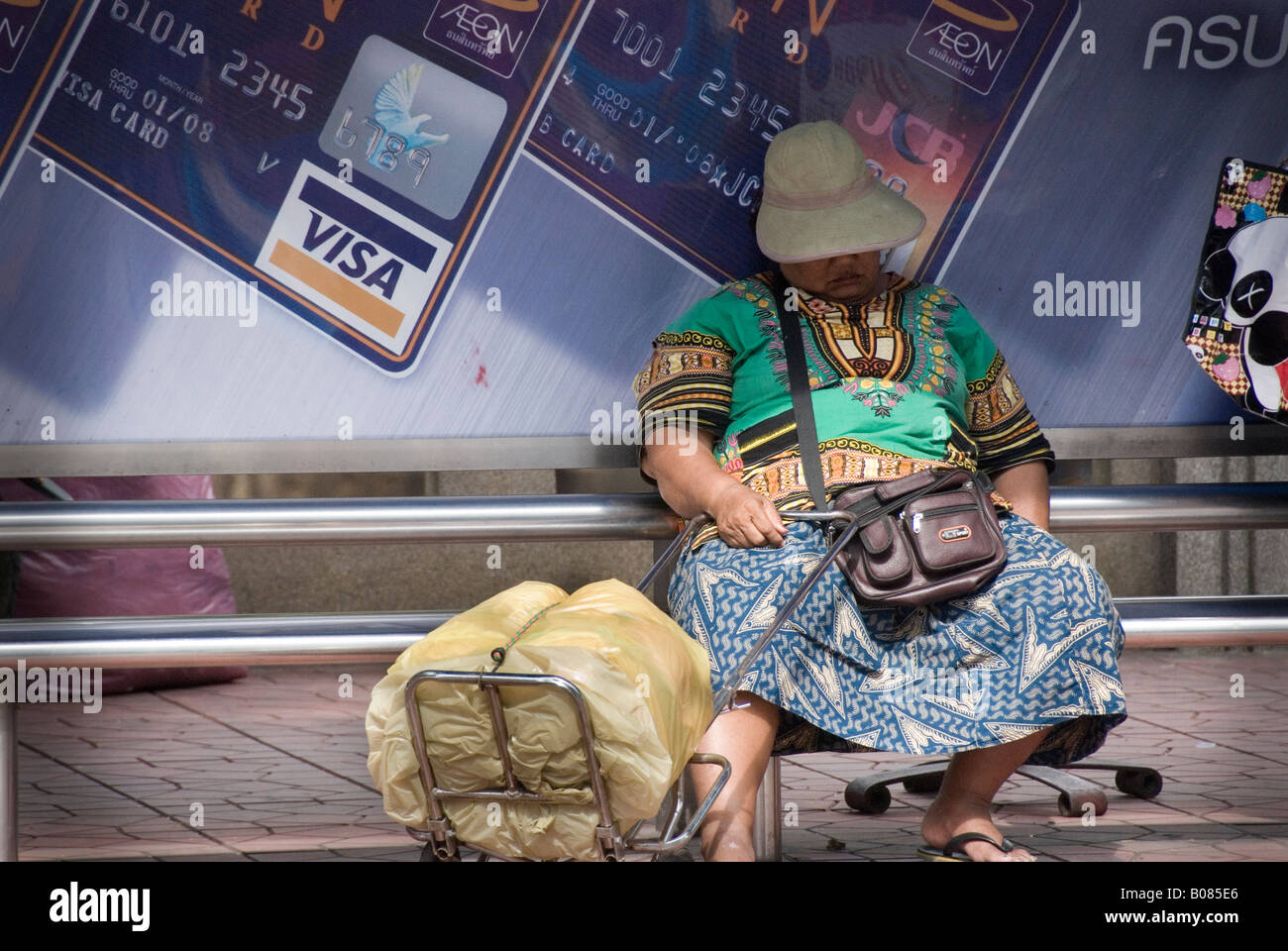 A homeless woman sleeps next to a Visa sign in Bangkok Thailand. Stock Photo