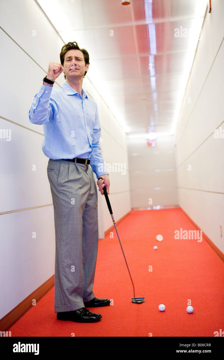 Businessman playing golf in office hallway Stock Photo