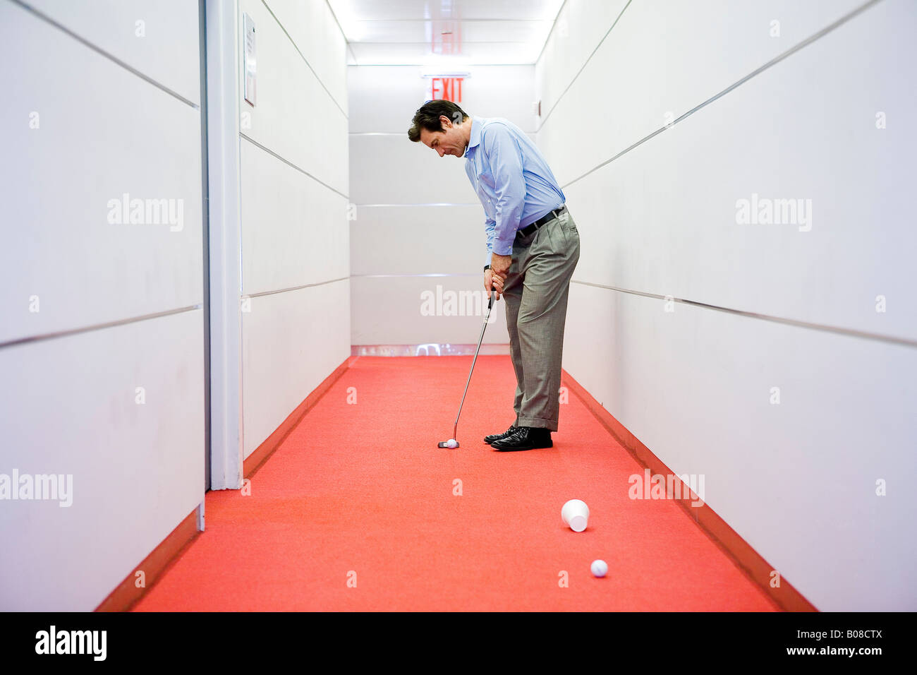 Businessman playing golf in office hallway Stock Photo