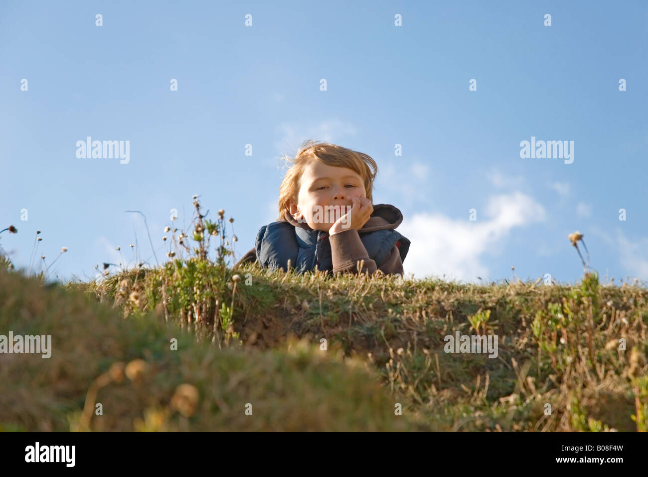 A happy 8 year old boy laying down on the grass and looking smug and ...